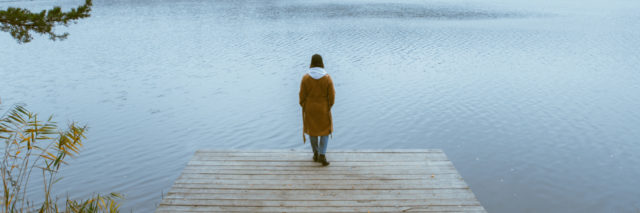 woman standing on a pier near a lake, focus on her back