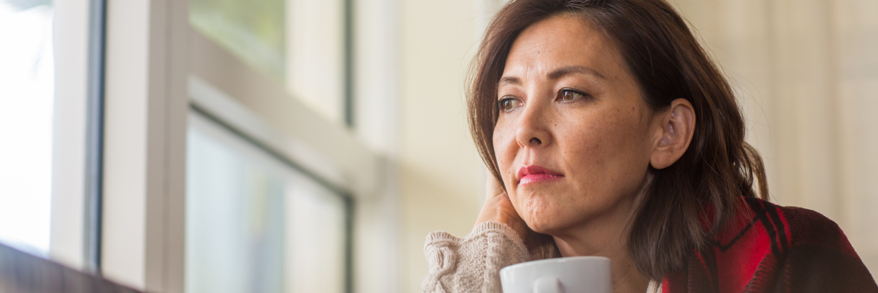 Photo of woman sitting by window wrapped in red blanket and holding mug