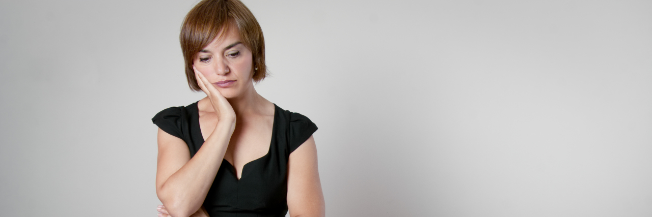 It Hurts to Not Feel Like You Have a Family During the Holidays worried woman with brown hair standing over a table about to set it with her hand on her face staring blankly