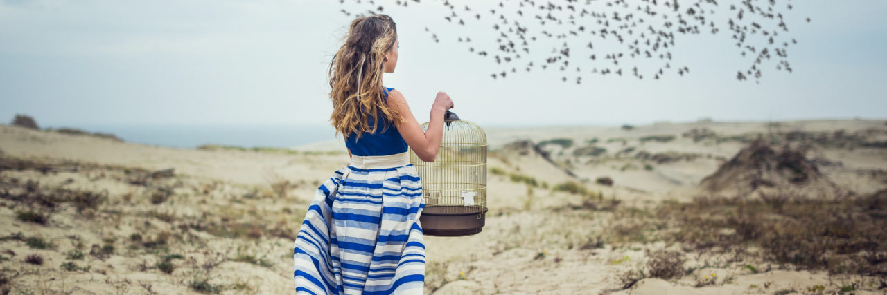 a young woman standing with a birdcage looking at a flock of birds in the sky