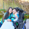 woman hugging a child in a wheelchair and smiling