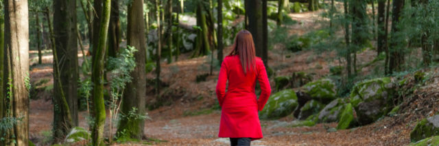 Woman walking away alone on a forest path wearing a red overcoat.