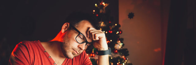 Tired man in red shirt with a Christmas tree in the background.