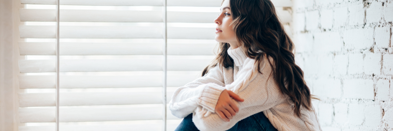 Read This If Struggling With Depression and Guilt This Christmas photo of young woman sitting on windowsill beside christmas decorations, hugging her knees