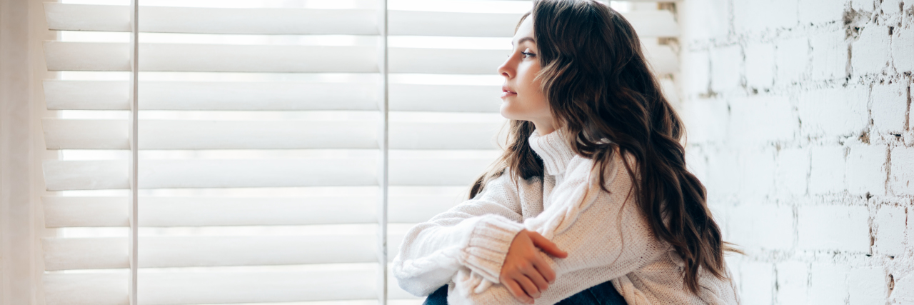 How to Balance Your Holiday Expectations When You're Sick young woman sitting on a windowsill near Christmas decorations