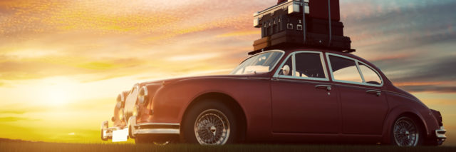 Retro red car with luggage on roof rack at sunset.