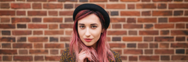 woman with pink hair in hat posing at wall