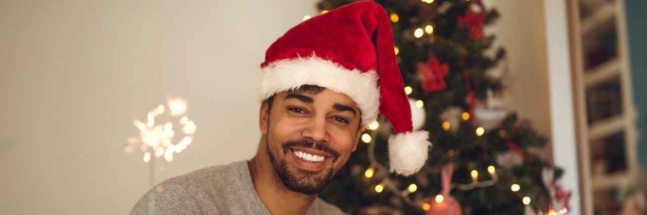 man in a santa hat in front of a Christmas tree holding a sparkler, smiling