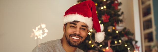 man in a santa hat in front of a Christmas tree holding a sparkler, smiling