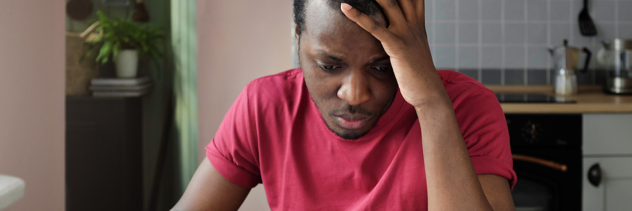 Young anxious worrying african american man looks desperately to bills, faces problems with paying taxes, holding head with one hand