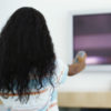 Rear view of a girl pointing a remote at a television.