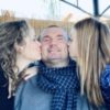 Jeff with his wife and daughter kissing him on each cheek.