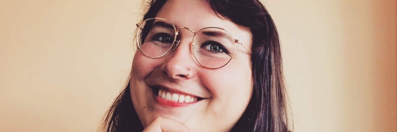 Photo of the writer, a younger white woman wearing glasses and smiling. Her hand is on her chin.