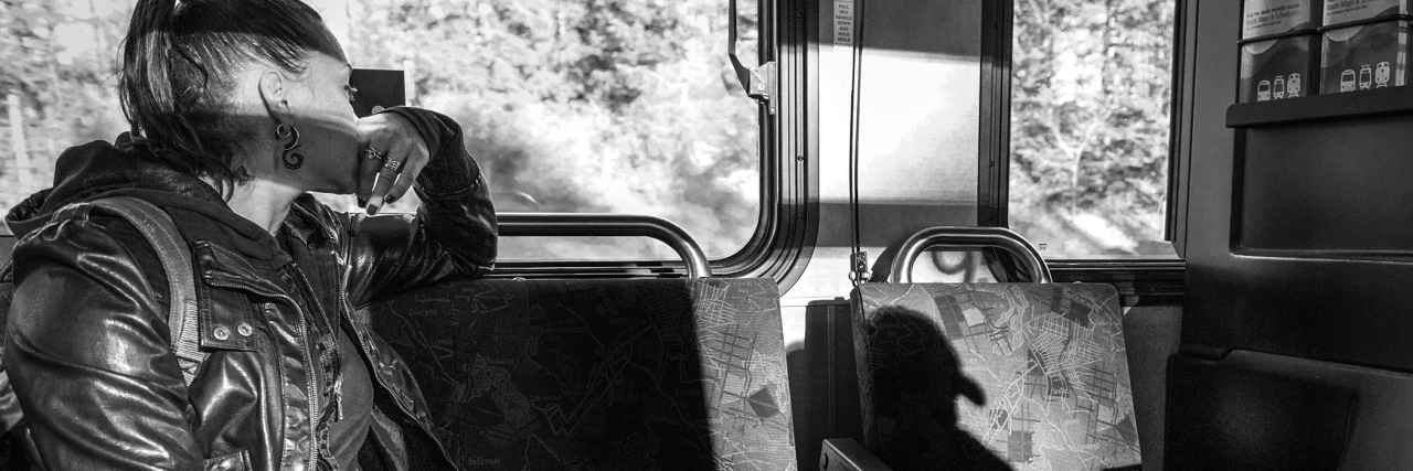black and white photo of woman sitting on bus with face hidden, casting a harsh shadow