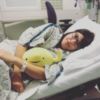 Woman laying in a hospital bed, wearing a hospital gown and holding a bladder stuffed animal