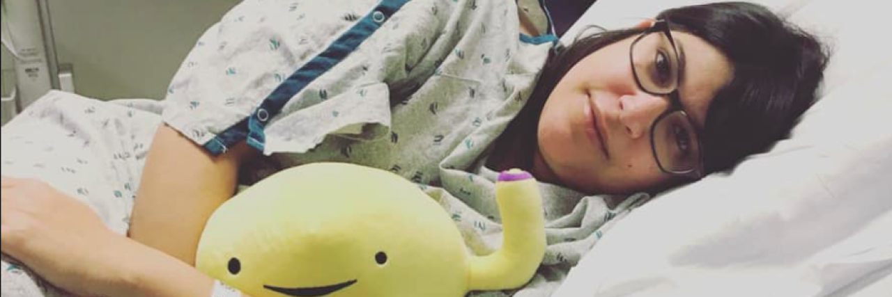 Surviving an InterStim Trial Woman laying in a hospital bed, wearing a hospital gown and holding a bladder stuffed animal