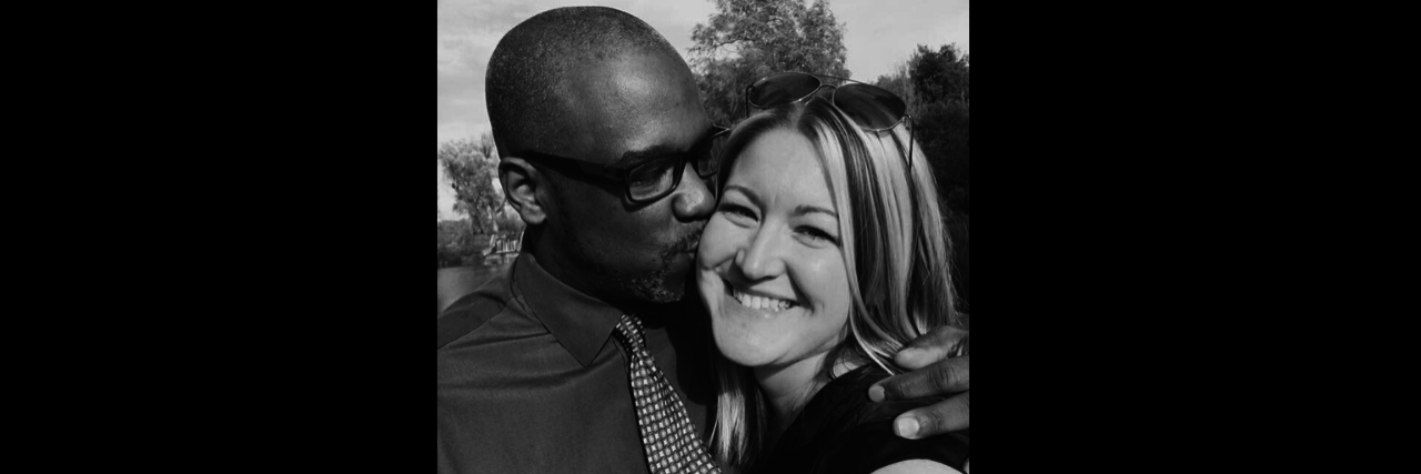 When My Daughter Complimented My Smile As a Chronically Ill Mom A woman stands smiling with a man next to her kissing her on the cheek