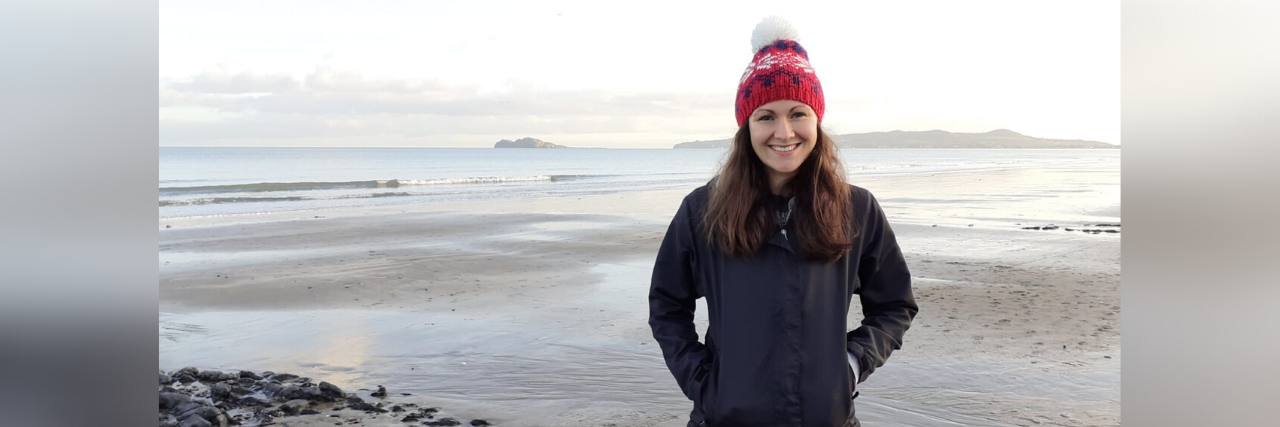 5 Ways I'm Practicing Self-Care Honestly Without a Therapist photo of author in a red hat and black jacket smiling at the camera in front of a lake/ocean