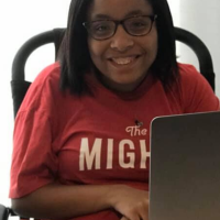 Mighty contributor Tylia Flores smiling for camera wearing her red Mighty t-shirt. her laptop in front of her