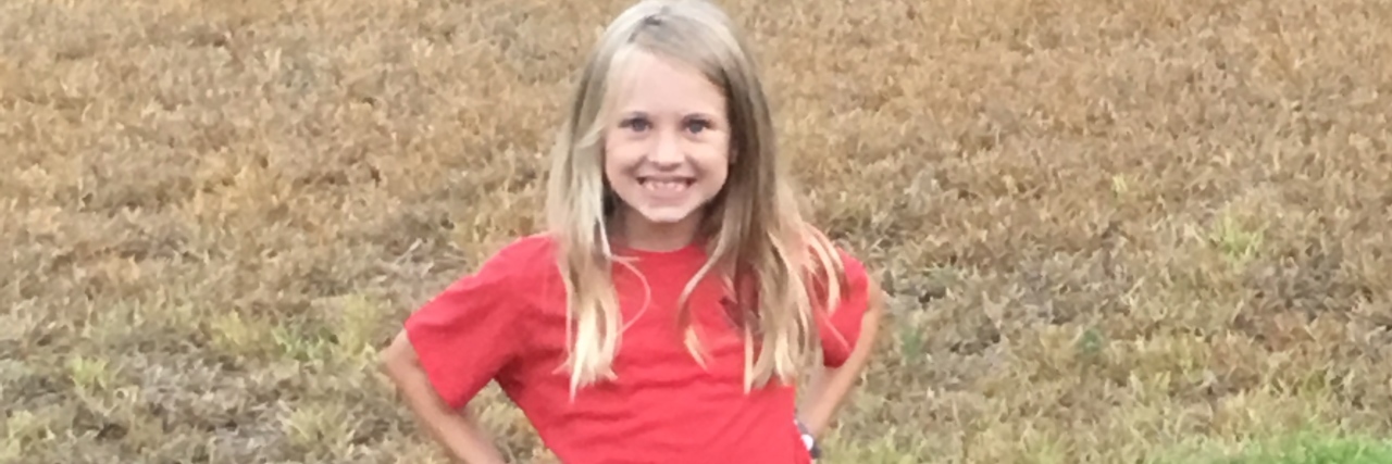 My Biggest Anxiety as a Mom to a Kid With Apraxia a little girl smiling wearing a red shirt and blue shorts