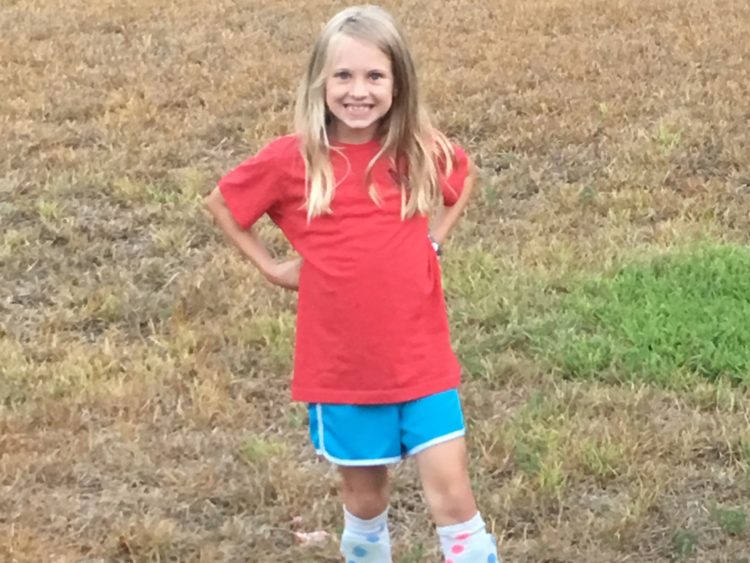 a little girl smiling wearing a red shirt and blue shorts