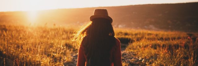 photo of woman standing or walking in field at sunset, facing away from camera
