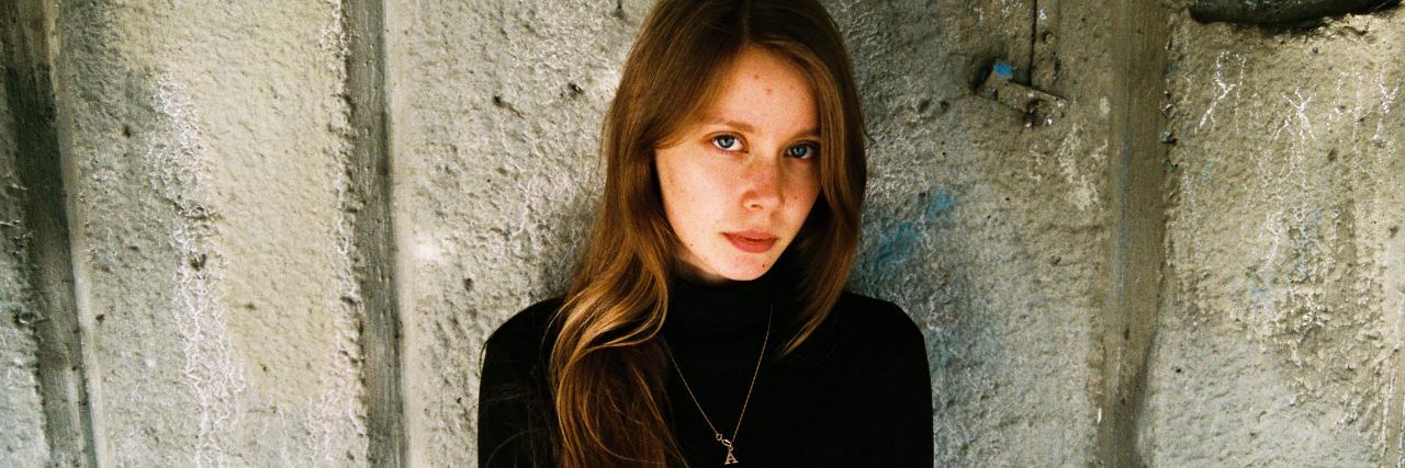 How My Psychiatrist Helped Me Understand I Was Actually Being Bullied photo of redheaded woman looking into camera with concerned expression, standing with her back against a concrete wall