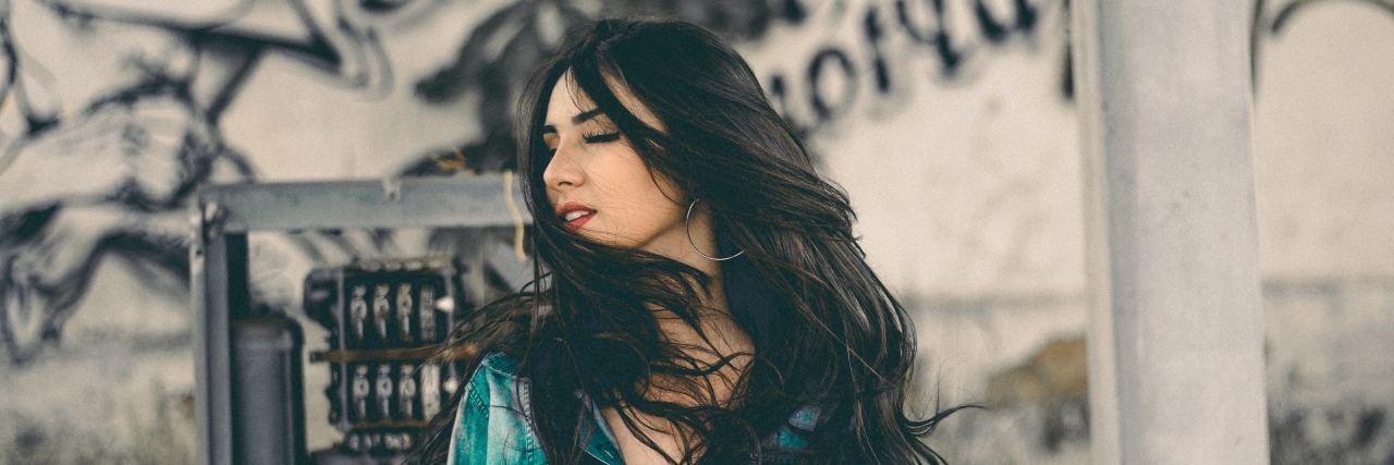 Guilt and My Family Keep Me From Dying By Suicide woman with black hair and a blue and white shirt looking to the side with her eyes closed and wind blowing her hair across her face