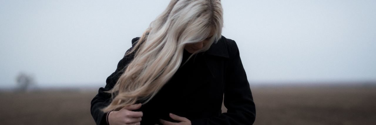 woman in a black jacket with long blonde hair looking down with her hair covering her face