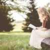blonde woman sitting outside reading a Bible in a field on a sunny day