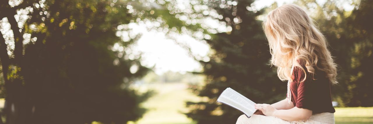 blonde woman sitting outside reading a Bible in a field on a sunny day