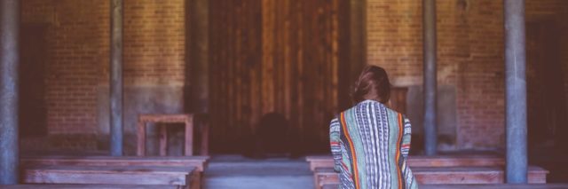 back of a woman sitting at a church alone in a pew