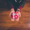 overhead photo of person's hands holding out red wrapped festive present with wooden floor underneath