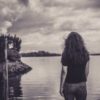 sepia tone photo of woman looking out at lake with trees on either side and in the distance