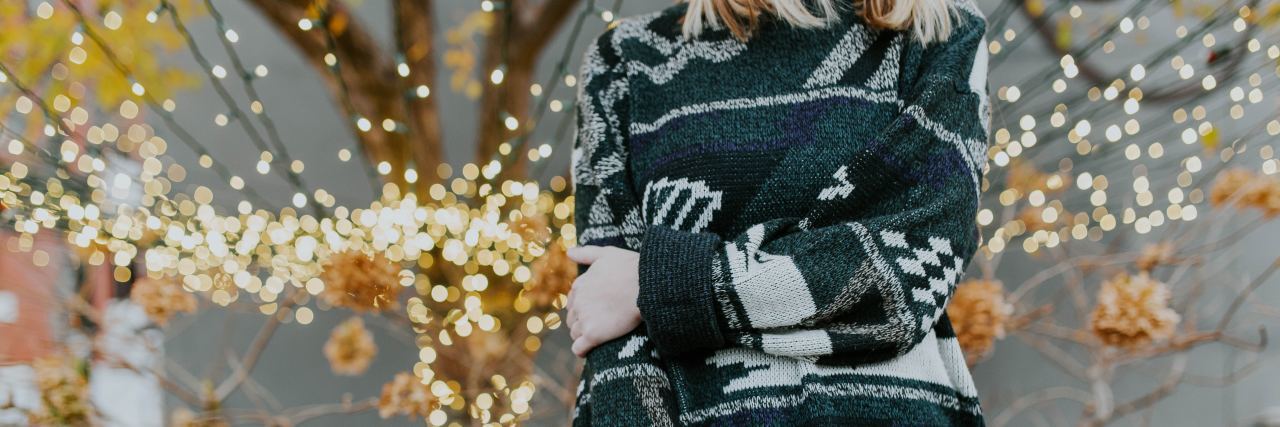 It's OK to Say 'No' to Holiday Events With Chronic or Mental Illness neck down picture of a woman in a green Christmas sweater standing in front of a lighted tree
