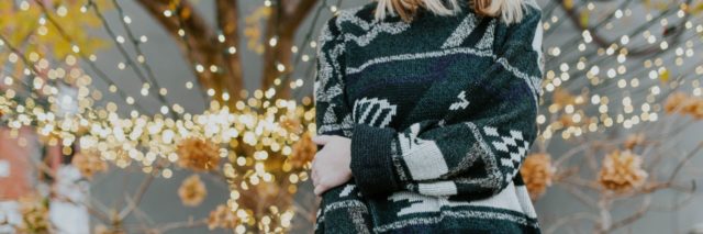 neck down picture of a woman in a green Christmas sweater standing in front of a lighted tree