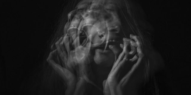 black and white distorted photo of woman screaming with her hands grasping her own face