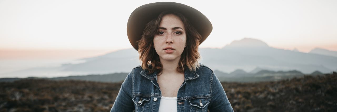 I Am More Than My Trauma, so Don't Define My Successes by It woman in a jean jacket and hat staring straight at camera with hands in her pockets