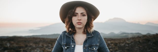 woman in a jean jacket and hat staring straight at camera with hands in her pockets