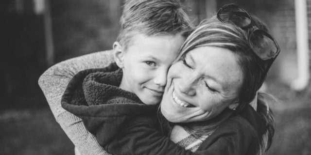 black and white photo of mother hugging son or woman hugging child with the boy looking into camera