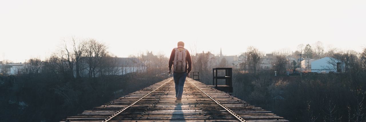 A Story of Childhood Sexual Abuse Leading to Familial Estrangement photo of a man on a railroad track walking with a backpack on toward the sunlight