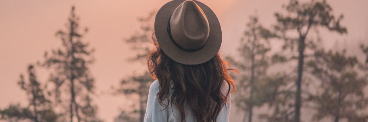 Learn to Forgive Yourself and Your 'Failures' This New Year’s photo of woman sitting on wall over valley looking out at sun and trees