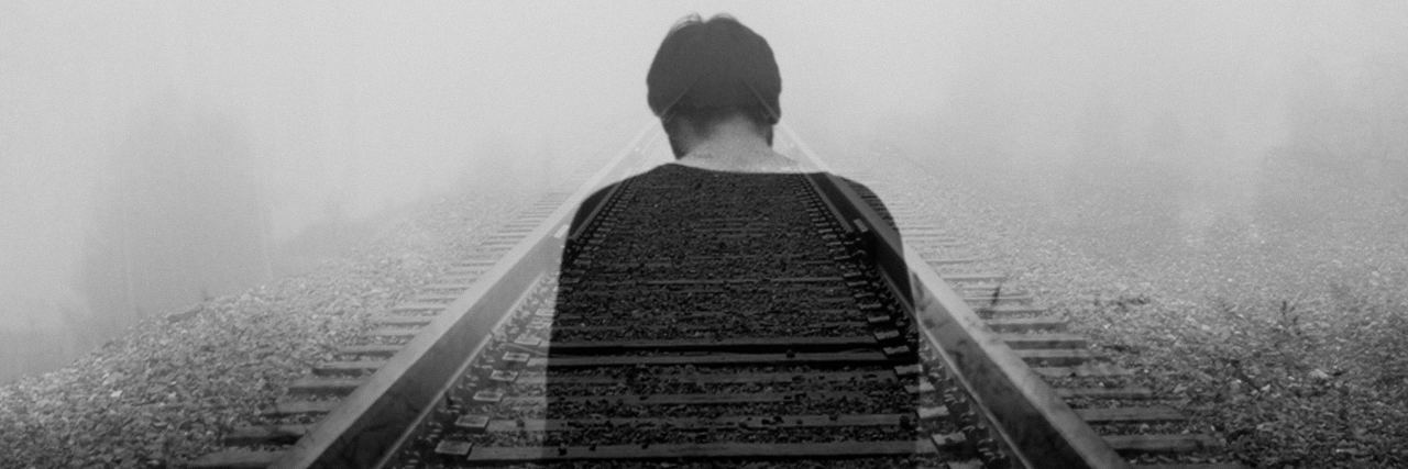 back of a transparent young man walking down train tracks