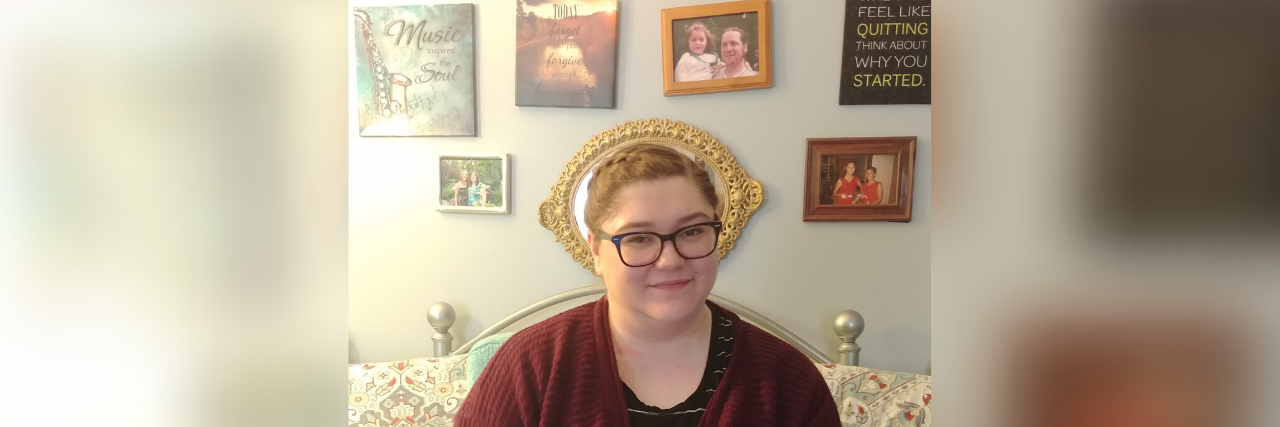 Finding Happiness Despite Mitochondrial Disease Grace sitting in bed with inspirational art on the wall behind her.