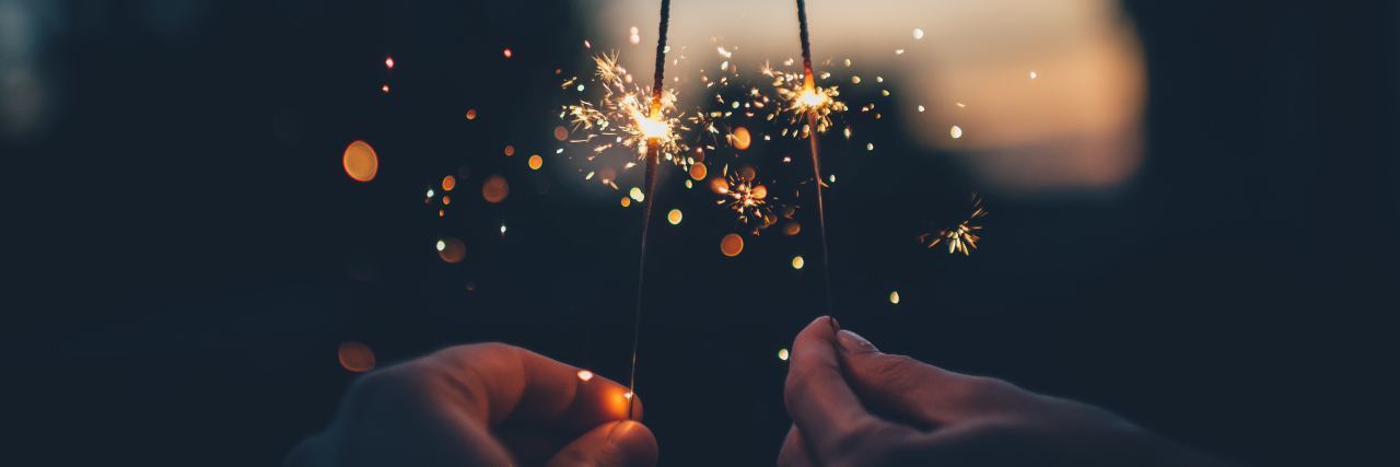 5 Achievable New Year's Resolutions If You Live With a Mental Illness 2 hands holding half lit sparklers outside at night