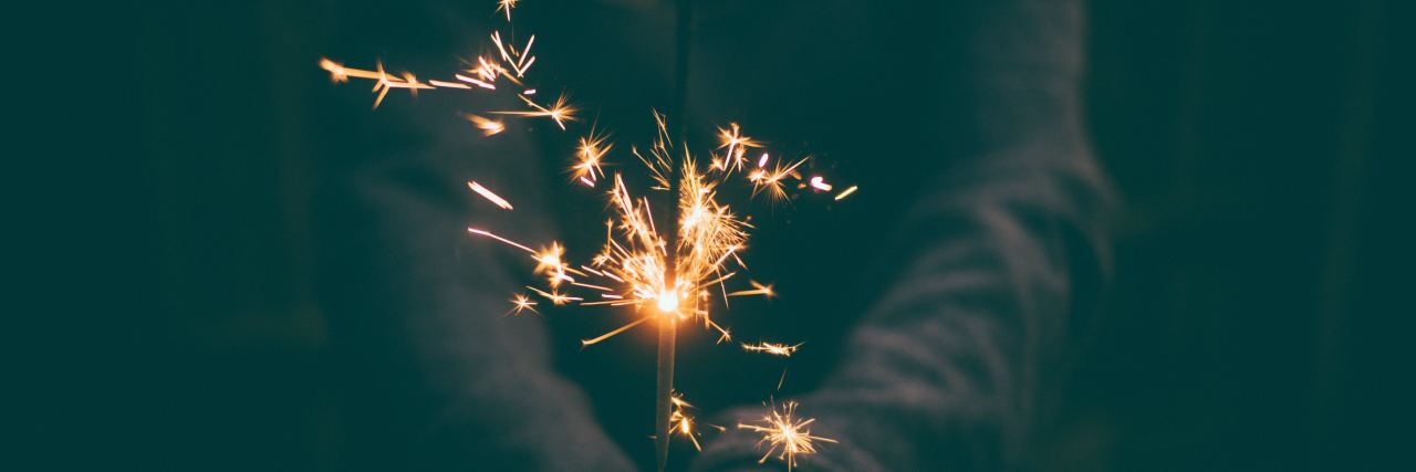 My Depression Makes It Hard to Find Hope in New Year's Eve dark picture of a woman in a gray sweater holding a sparkler