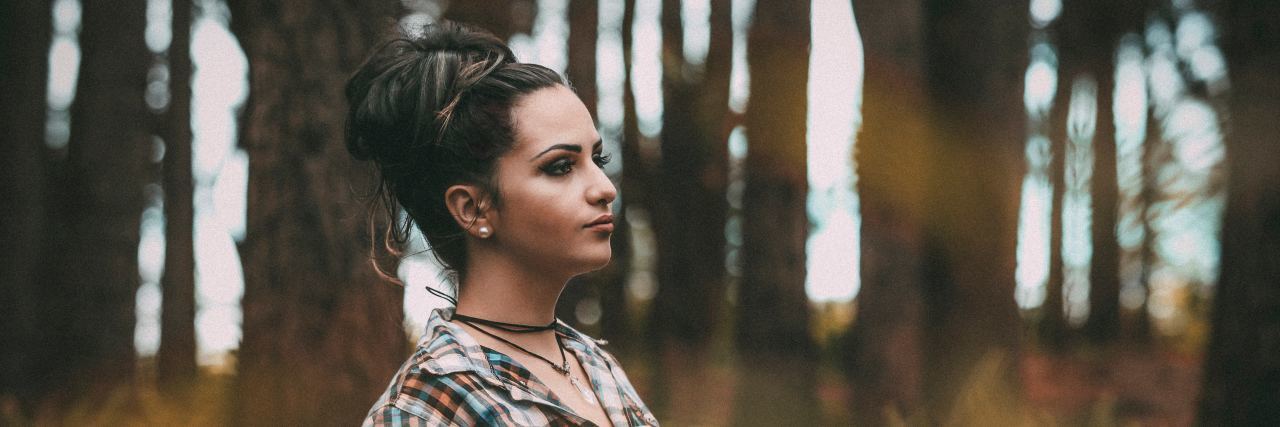 We Need to Be Careful With the Label 'High-Functioning' Mental Illness woman in a forest leaning against a tree with a straight face, hair in a bun and makeup on