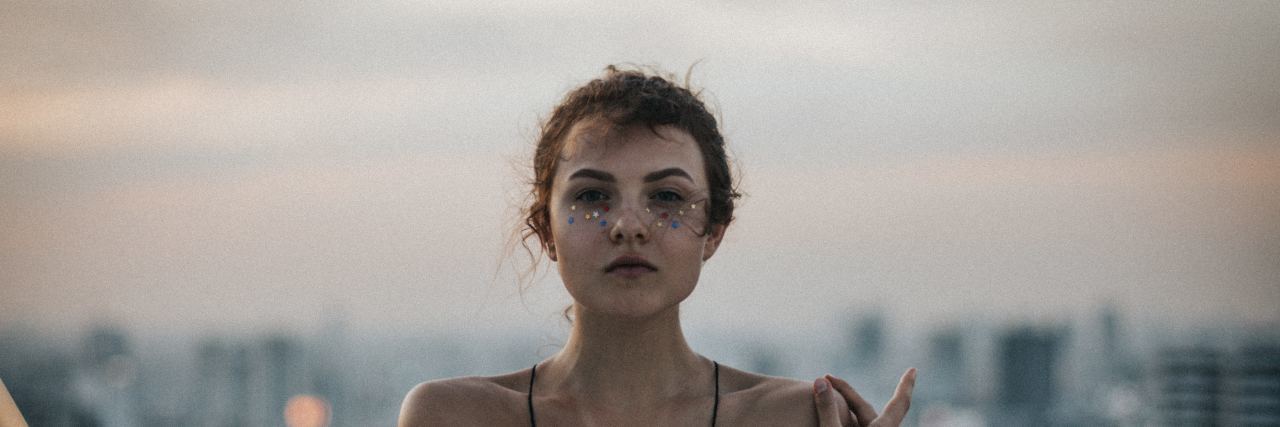 Realize the Reality of Mental Illness Before Saying Suicide Is Selfish young woman staring at camera seriously with a straight face and her arms wrapped around herself