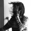 black and white photo of woman's hair being blown in wind in front of door, while she covers her face