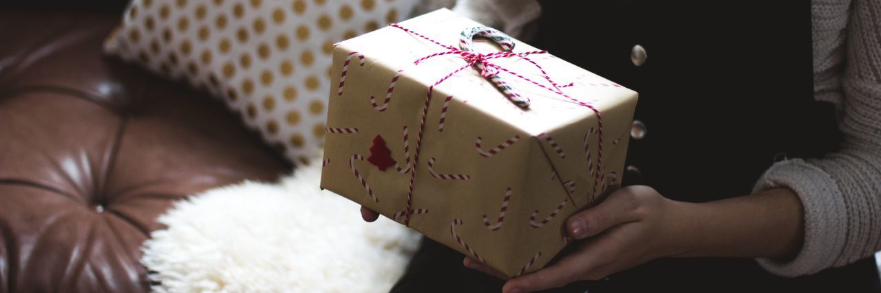 7 Gift Ideas for the Person in Your Life Who Is Grieving woman in black overalls sitting on a couch golding a brown paper package wrapped in red string